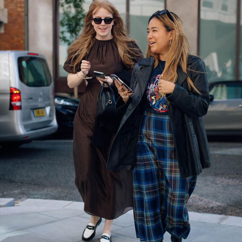 Two women talk and walk in the streets of London while wearing fashionable outfits. 