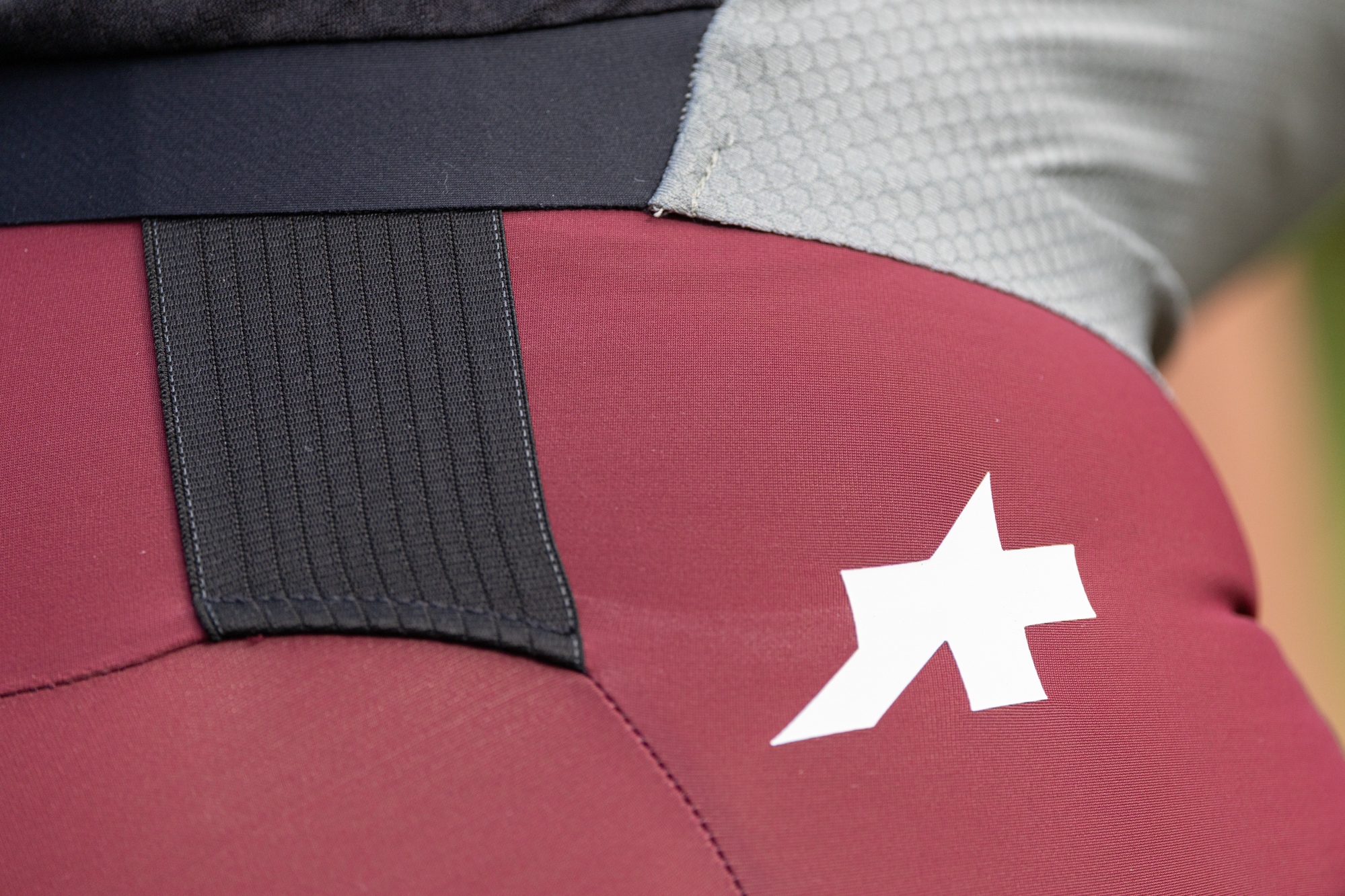 close up of the rear of a green cycling jersey and red shorts, showing the extended black strap and white Assos logo