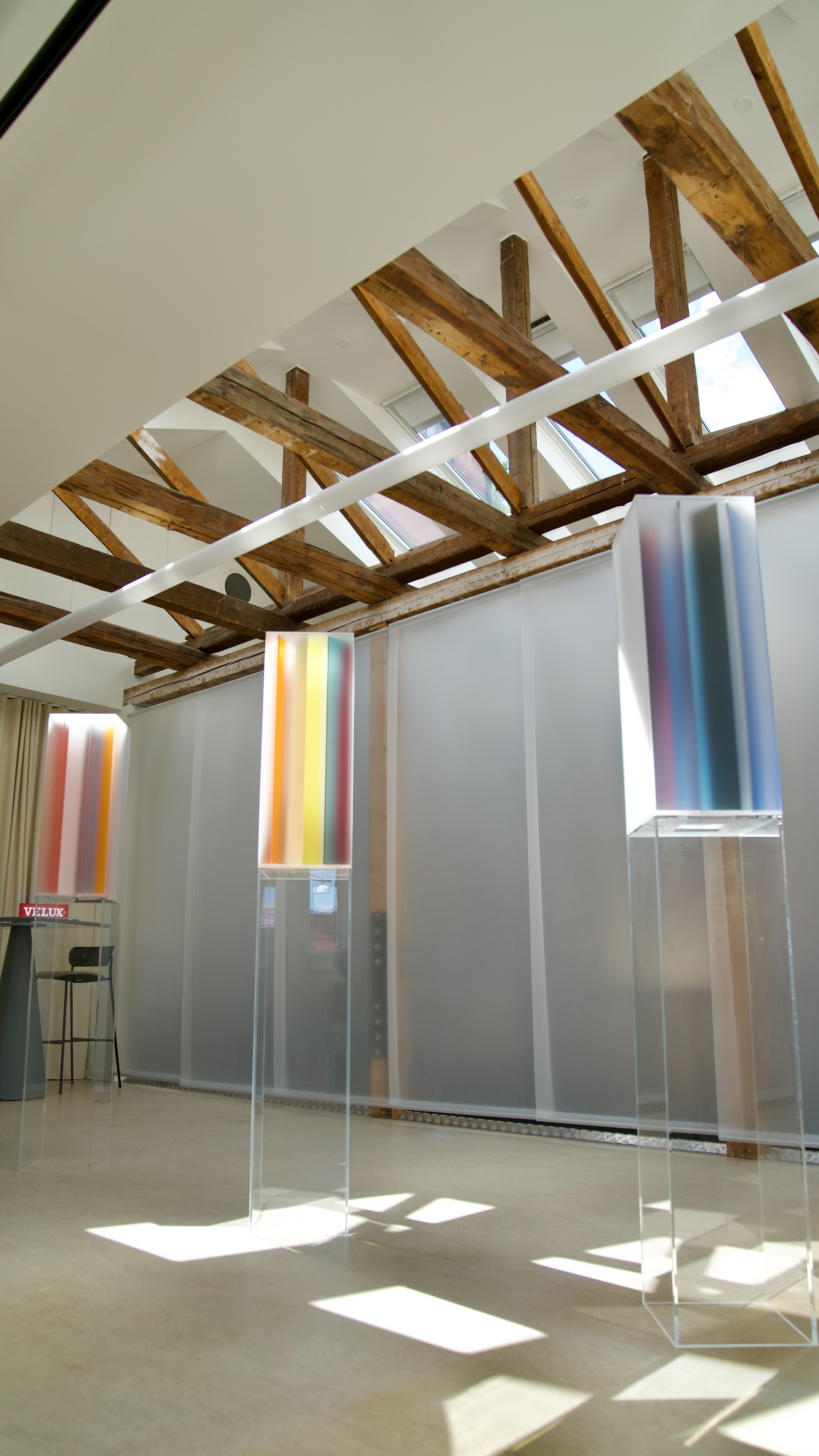 Installation view of an exhibition featuring gradient sculptural pieces made of opaque glass in different tones, placed atop transparent pedestals.