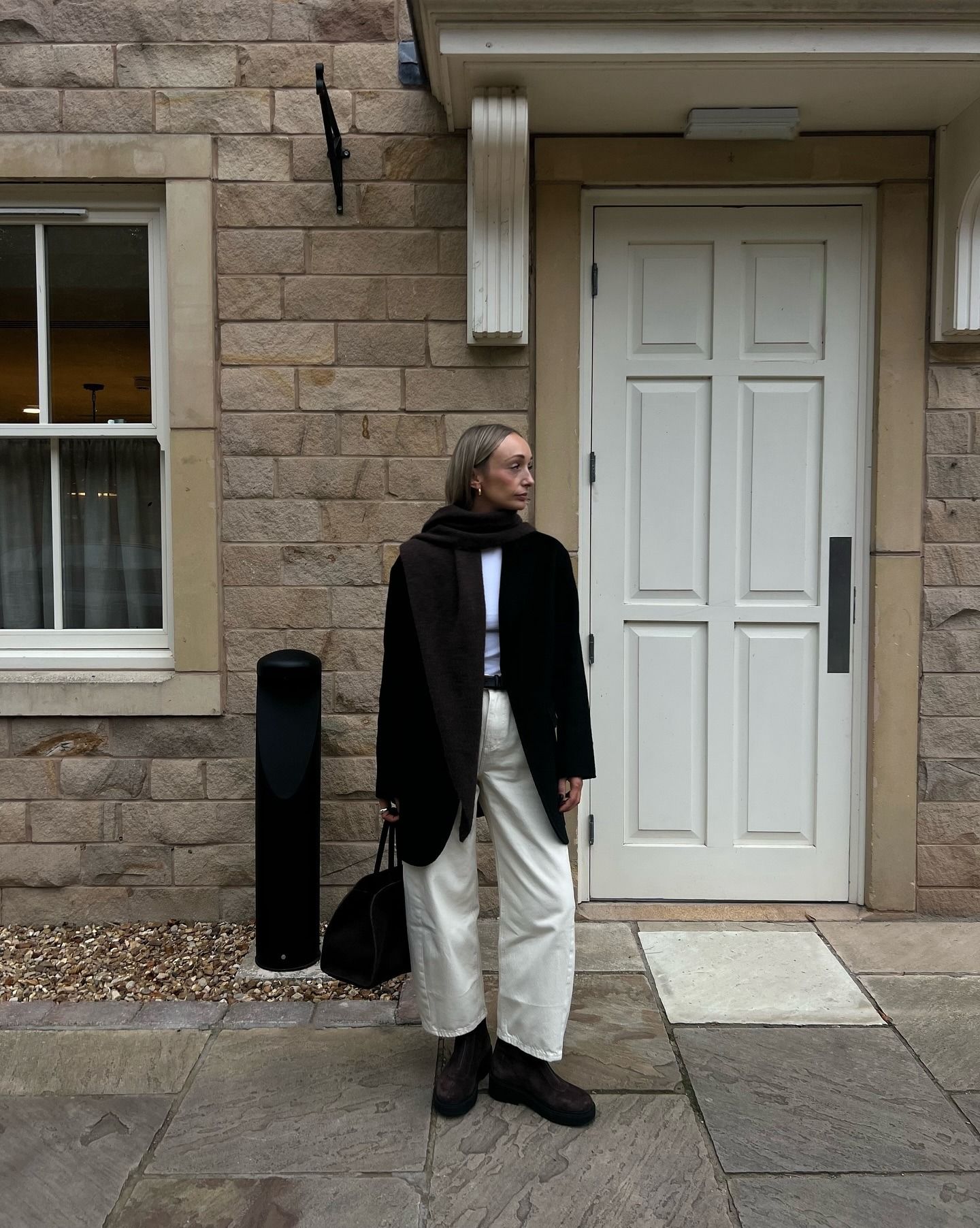Stylist Danielle Ward wears M&S white jeans and brown suede boots posing against a doorway in autumn