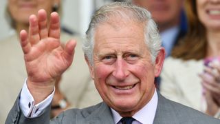 King Charles III waving and smiling with a grey suit on