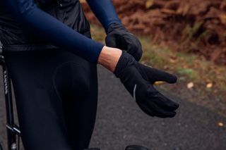 Image shows a rider putting on gloves to avoid cold hands while cycling.