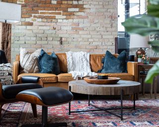Industrial-rustic living room with round wood and metal coffee table, mustard sofa and exposed brick wall