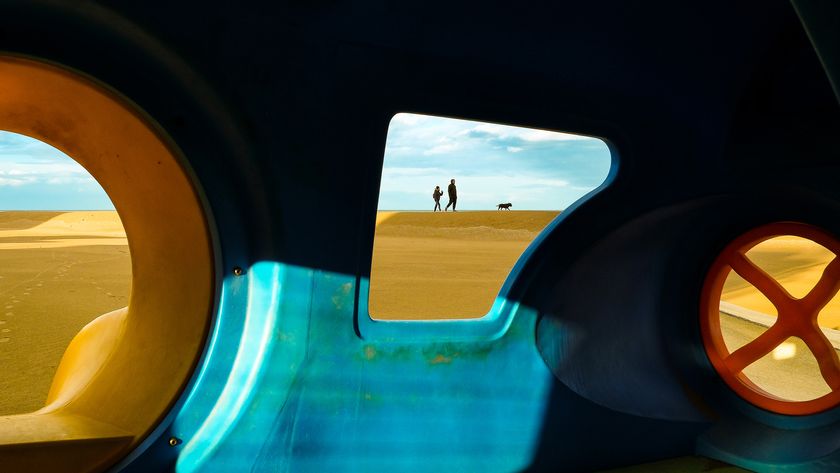 View through colorful playground tunnel framing a couple with a dog on dunes under a blue sky. Bright, playful, and serene atmosphere