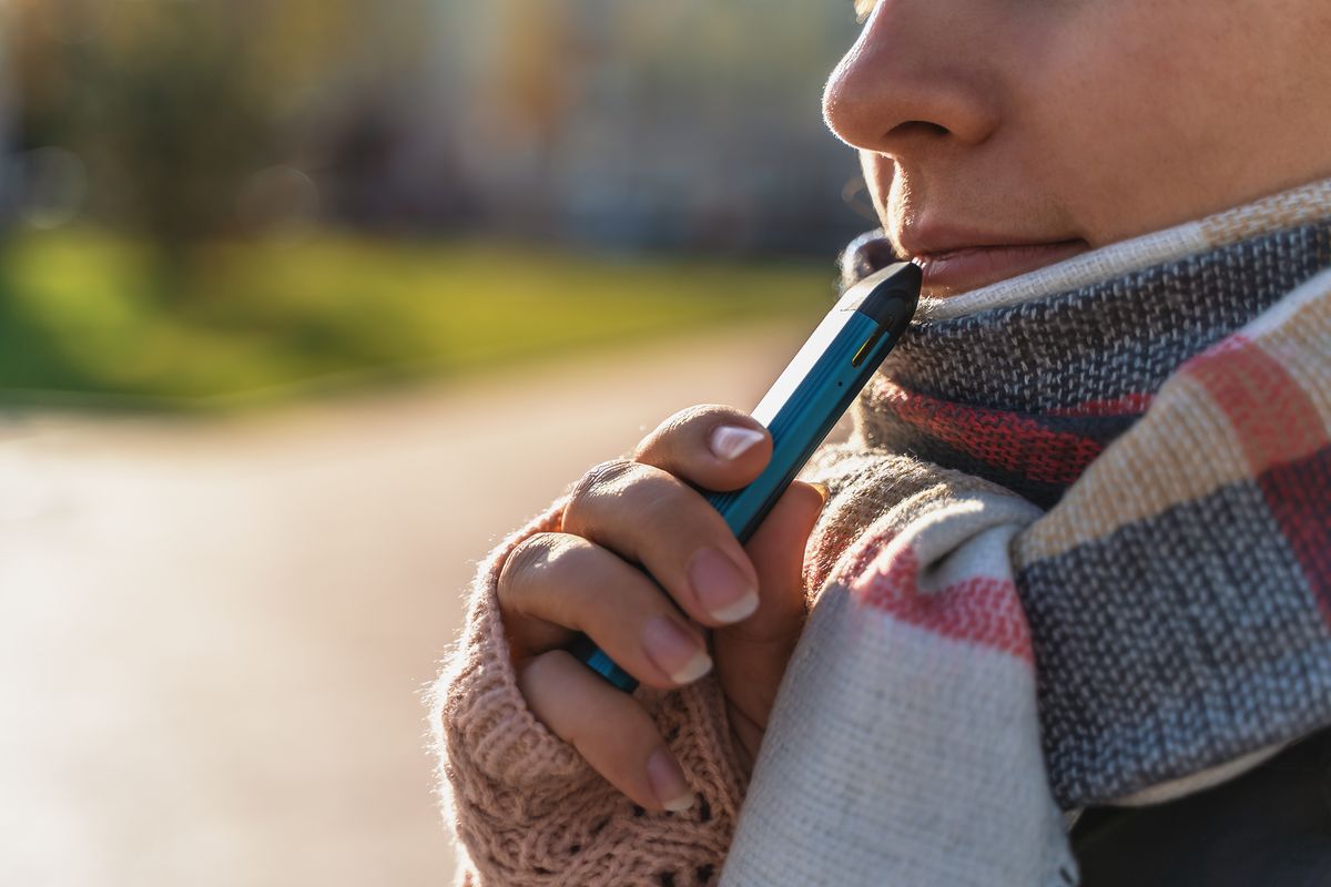 A young person vapes a &quot;pod-mod&quot; style e-cigarette.