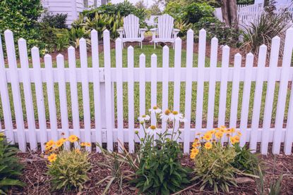 white picket fence and flowers in front of a yard and lawn chairs