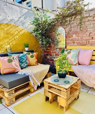 A raw pallet coffee table in backyard decorated with wall paint decor and outdoor cushions