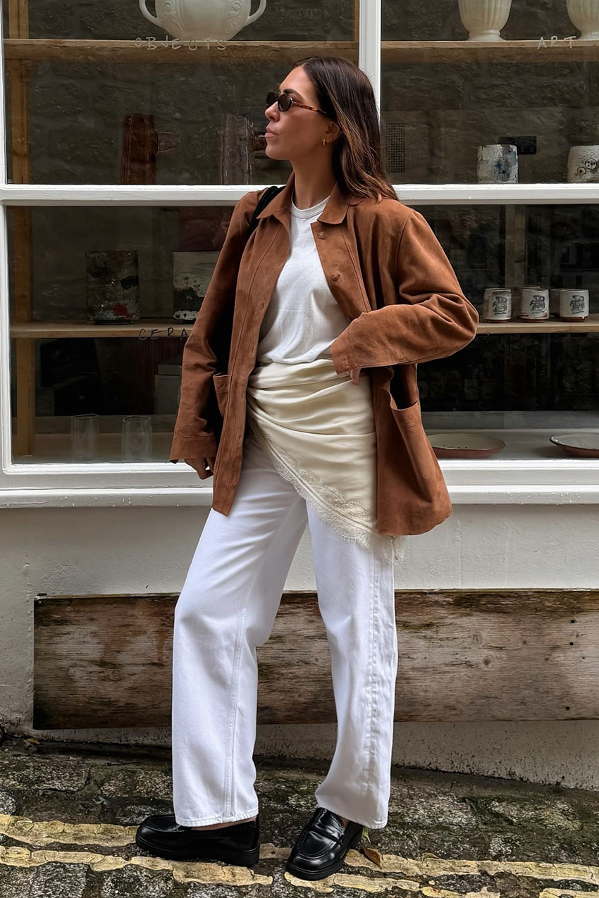 a woman wearing a brown jacket, white tee, white jeans, black loafers, and lace-trim scarf