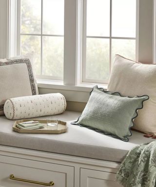 throw pillows in muted green and cream and patterned bolster on a day bench