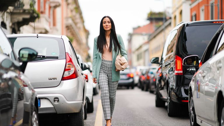 A woman walks in the street wearing a pale green blazer and striped pants