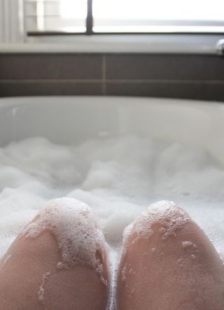 A person taking a bath in a white tub with just their knees visible through the bubbles