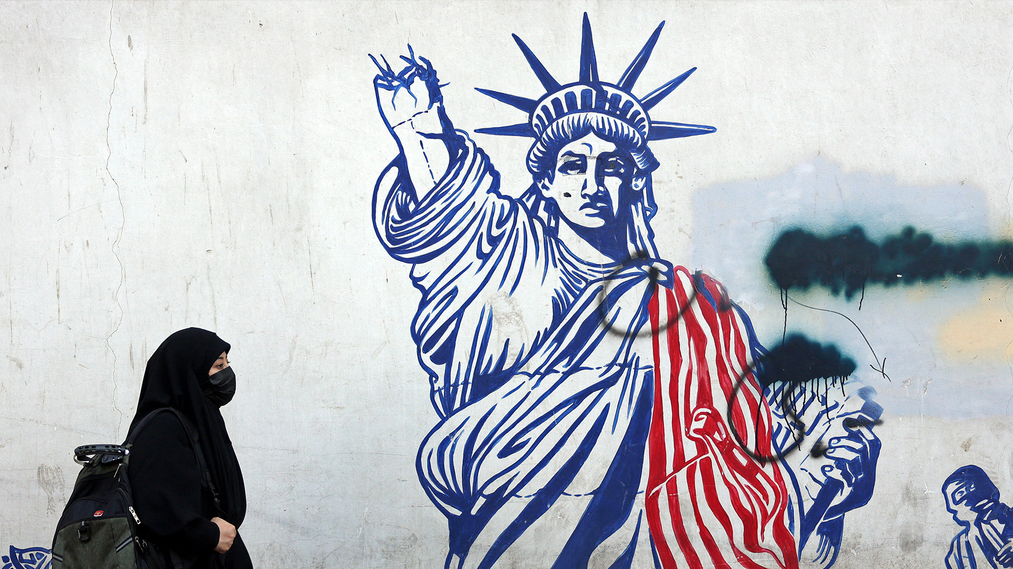 A veiled Iranian woman walks past an anti-US mural next to former US embassy in Tehran, Iran