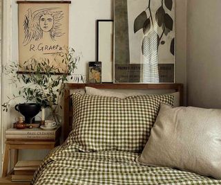 Piglet in Bed Botanical Green Gingham Bed Sheets on a bed beside a nightstand with a potted plant against a white wall.