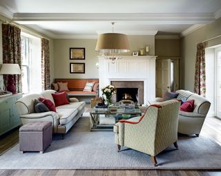 Sitting room with painted khaki walls, wooden floorboards, sofa and armchairs on cream rug, eggshell cabinet and fireplace.