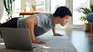 A man doing a push up in front of a laptop at home