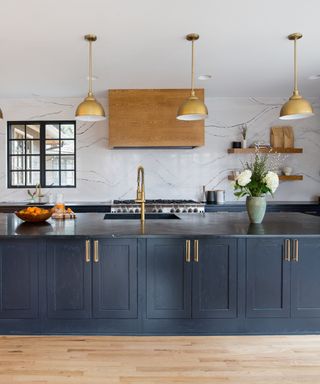 blue and marble kitchen with marble wall, blue cabinetry, hardwood floor, copper pendant lights, black countertop, open shelving, glazed wall units,