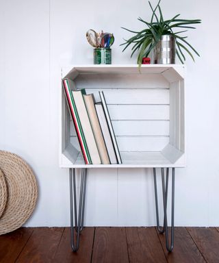 A white wooden bookshelf with books in it and a plant on top of it