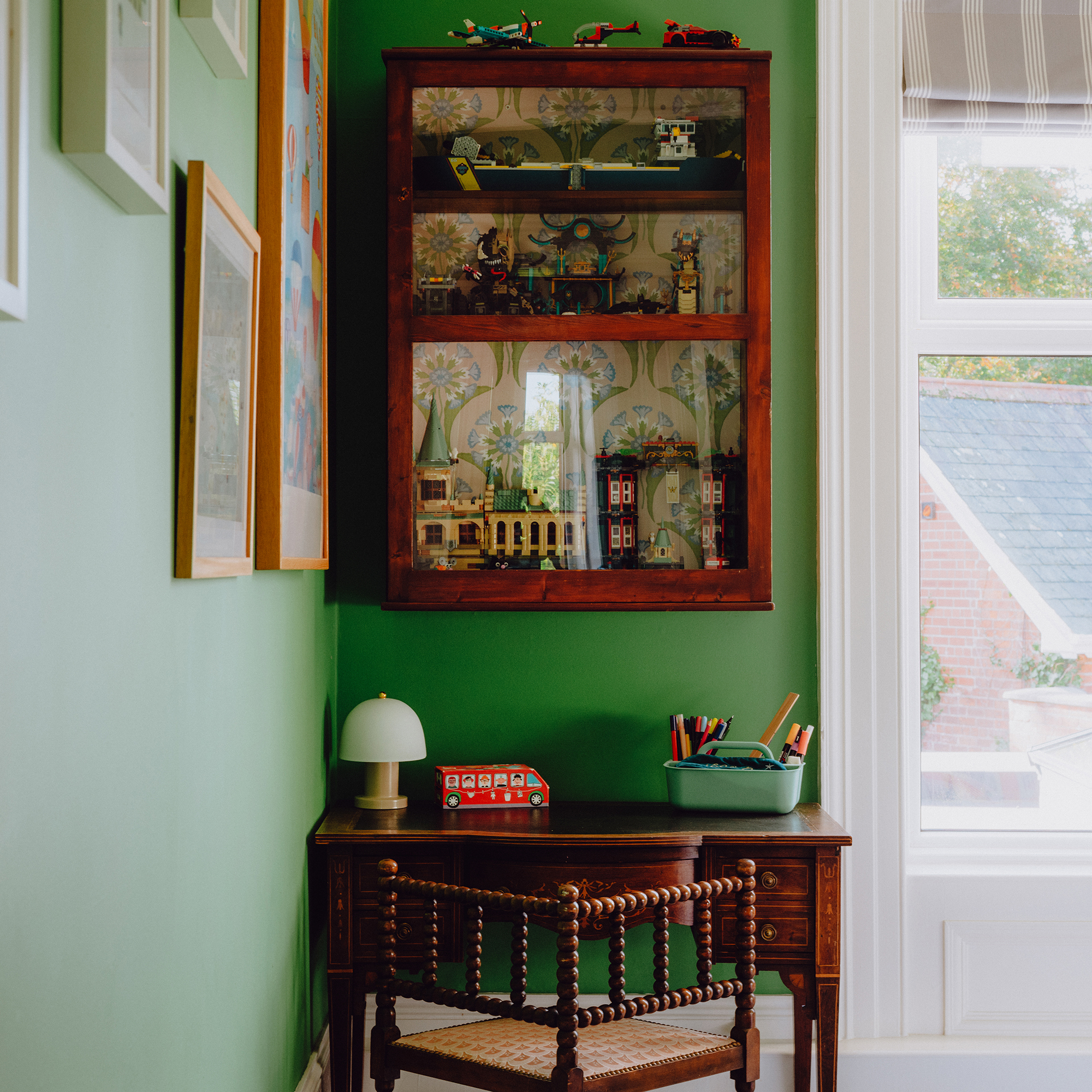 corner of a green bedroom with a small dark wood antique desk and glazed wall cabinet