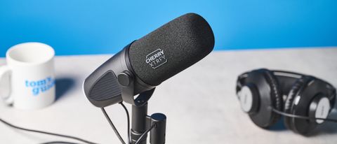 a black microphone by cherry XTRFY with a branded muff and an XLR and USB-C port sits atop a pale brown desk with a dark blue background