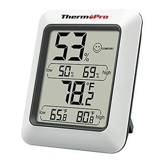 A white framed square digital hygrometer with large number display propped up on a small back stand