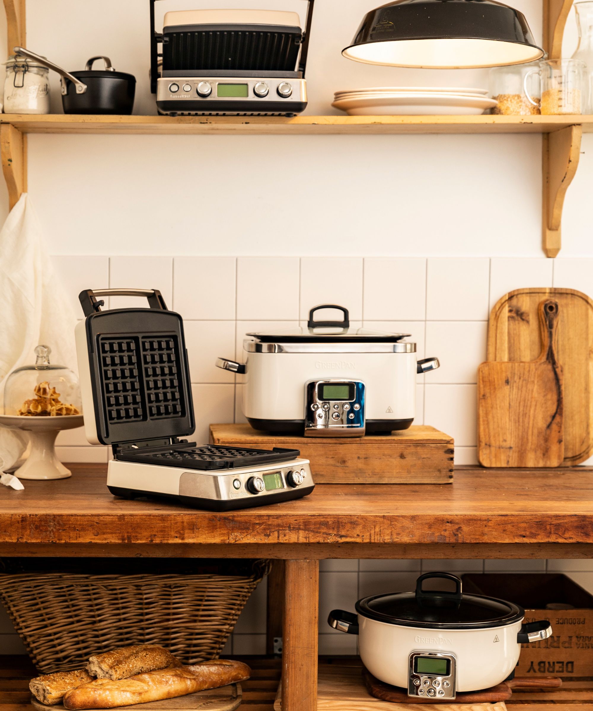 A kitchen counter featuring several cream coloured kitchen appliances, including a slow cooker and a waffle maker
