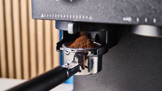 a black espresso machine by kitchenaid photographed against a blue background with silver chrome buttons and a pressure dial and steam wand