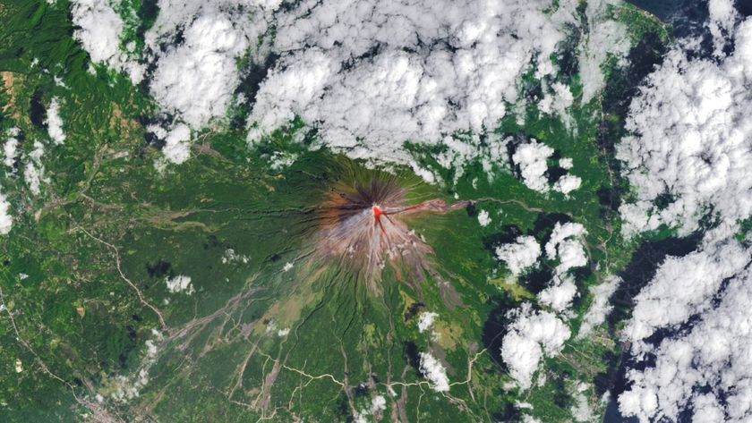 clouds float above a green landscape, in the center of which is a tall cone-shaped mountain with a bright red circle at its peak