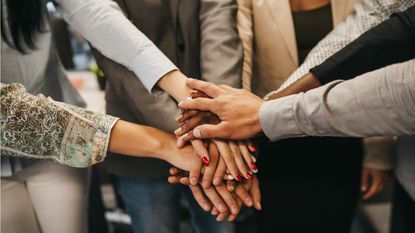 Employees stand in a circle and stack their hands in the middle to boost morale.
