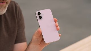 A person holds a dummy unit of the iPhone 16 in a pale pink color.