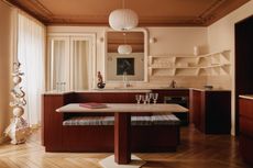 a contemporary kitchen with built-in banquette seating attached to the island with a creame and burgundy color scheme and parquet wood flooring and rust painted ceiling