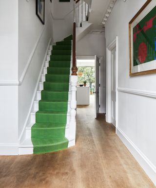 Narrow hallway ideas shown with white walls, wood floor and green stair carpet.
