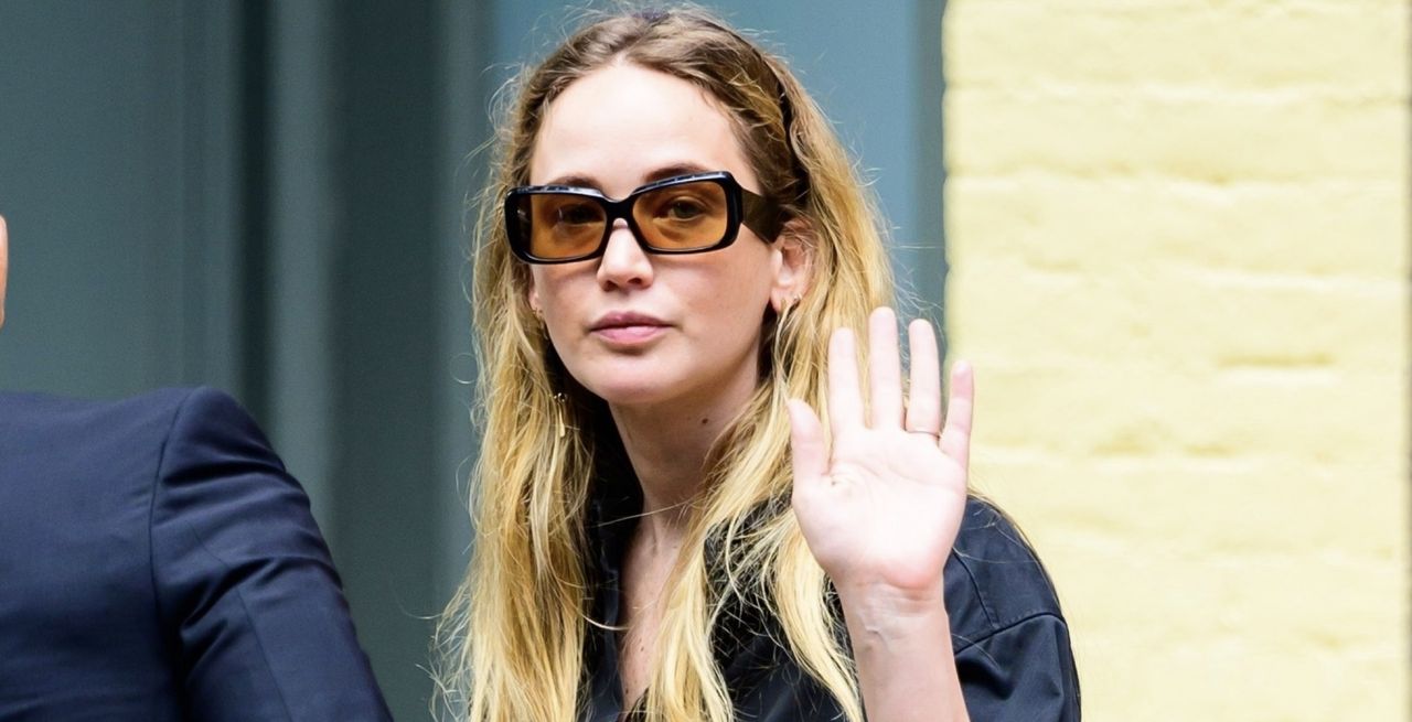 jennifer lawrence in new york city wearing a navy button down shirt and matching pants with tinted sunglasses, waving to the camera