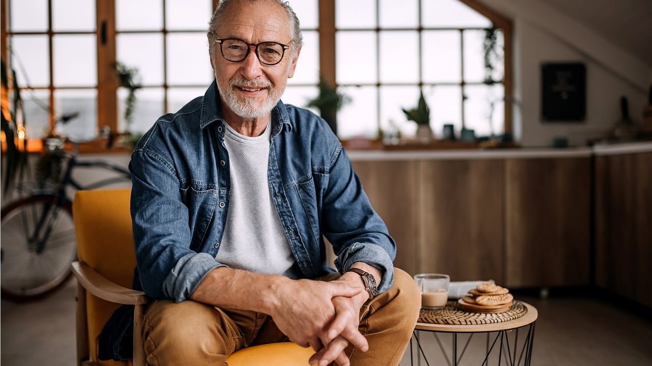 An older man sits in a chair smiling and looking happy.