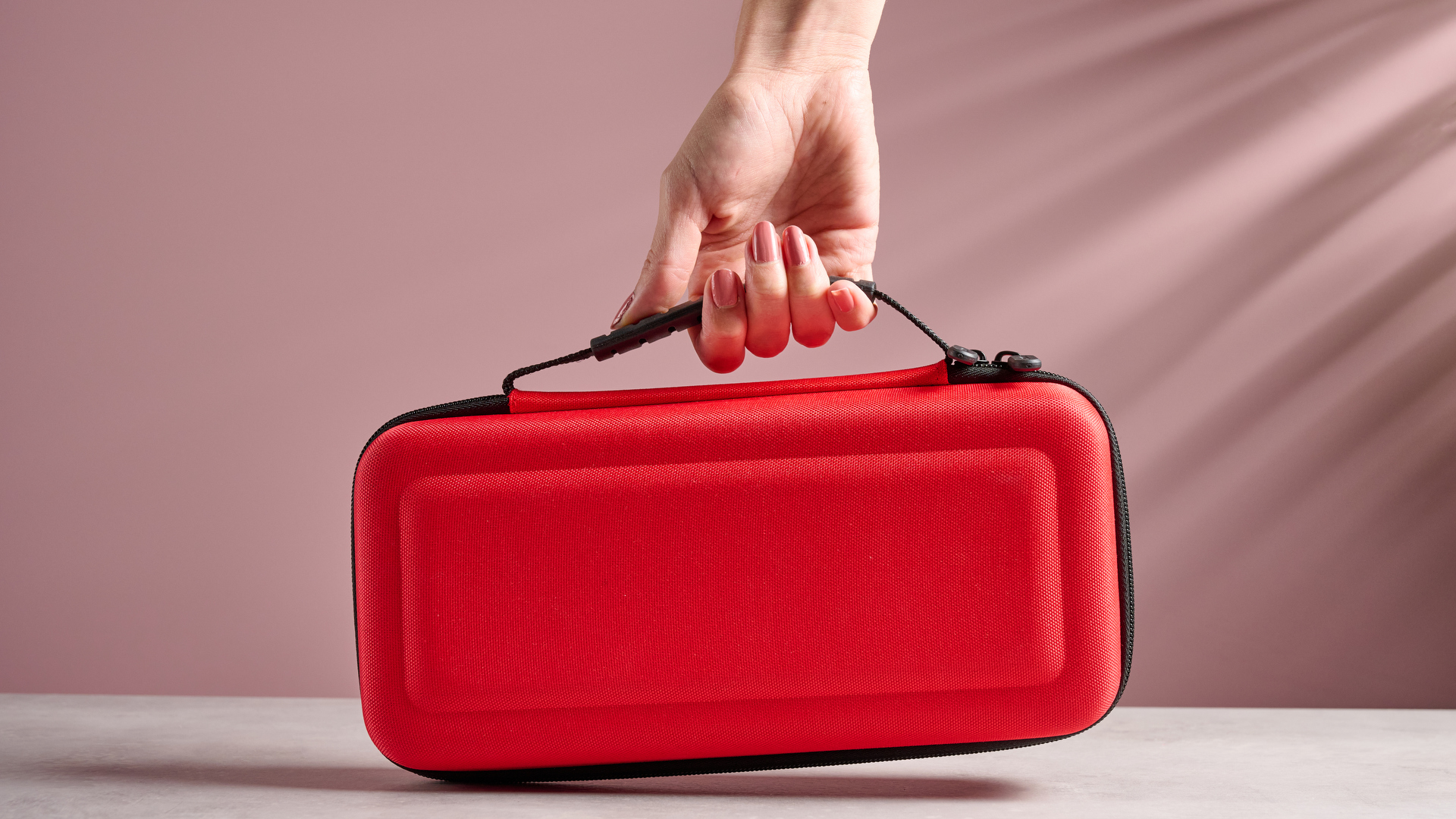 A woman's hand holding the Nacon Hard Carrying Case for Nintendo Switch 2 by the handle.
