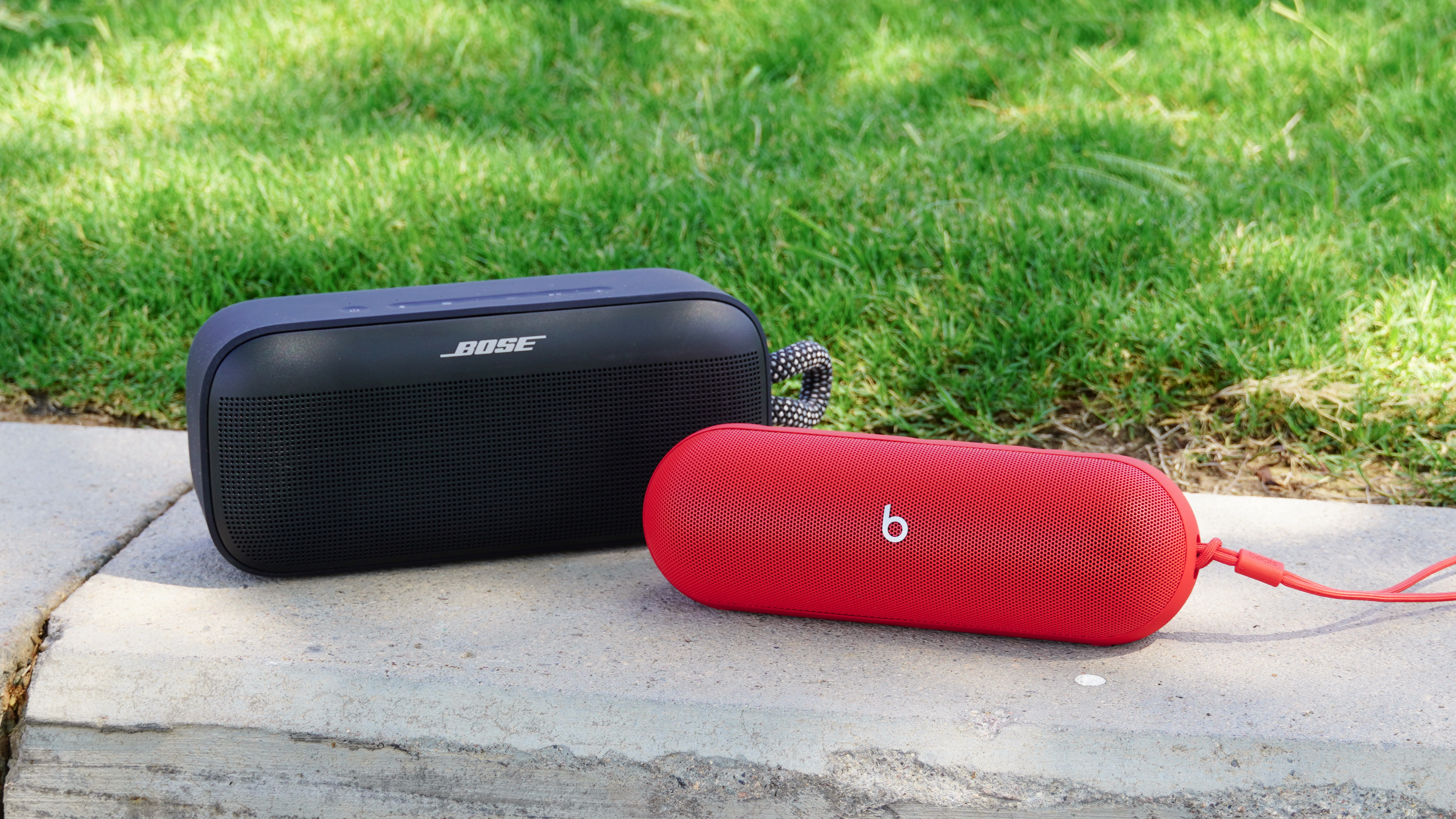The Bose SoundLink Plus (black) beside the Beats Pill (red) on a slab of concrete.