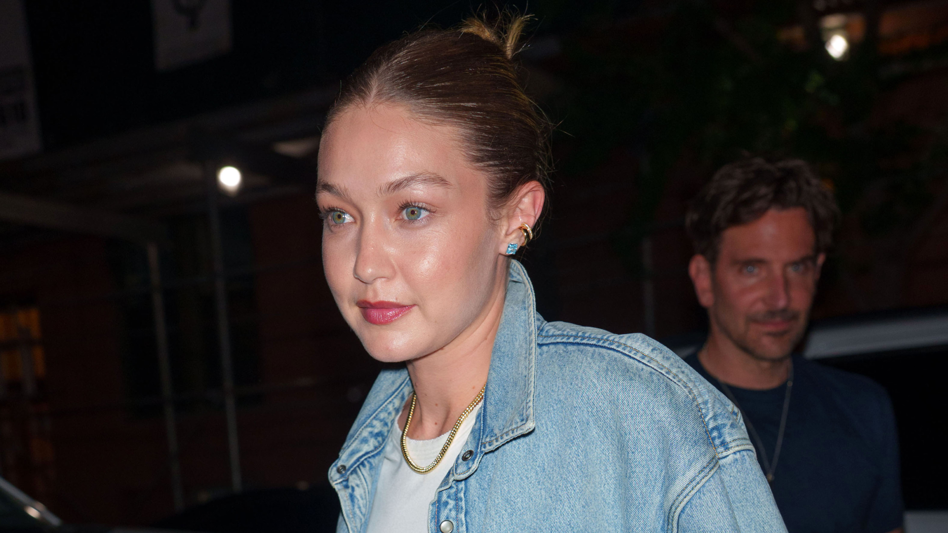 Gigi Hadid wearing a denim jacket, metallic track pants, and mesh flats