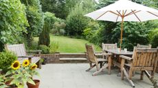 Patio in foreground of garden with bench and table and chairs to the side