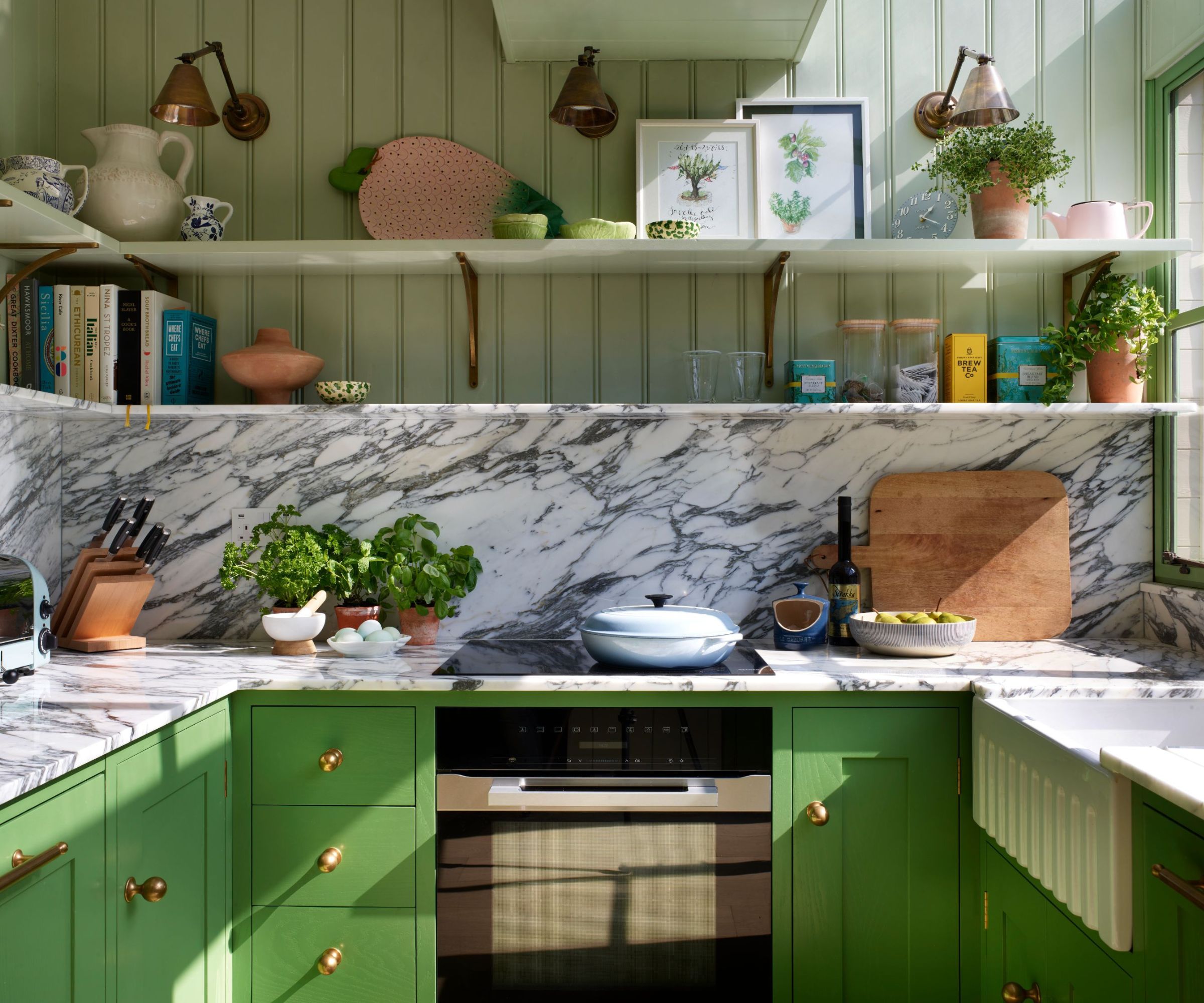 A green kitchen with marble countertops, paneled walls, and open shelving in place of upper cabinets
