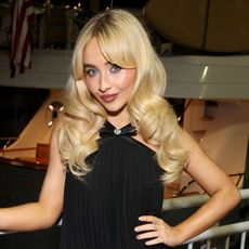 Sabrina Carpenter wears a black dress and poses with her hand on her hip