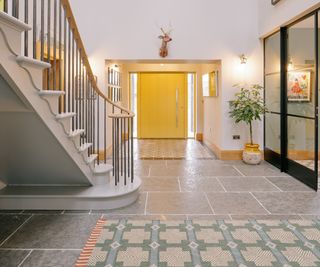 Hallway with curved staircase, yellow front door, patterned rugs, stag head and stone flagstone floor.