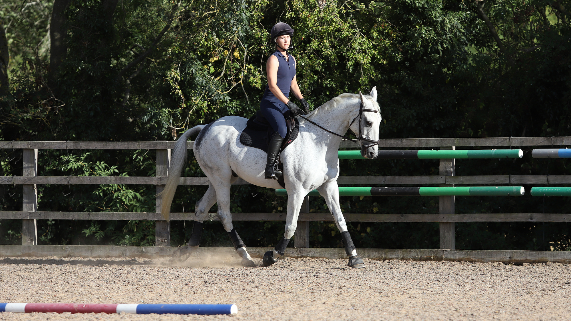 Rider on grey horse in arena with pole in the foreground