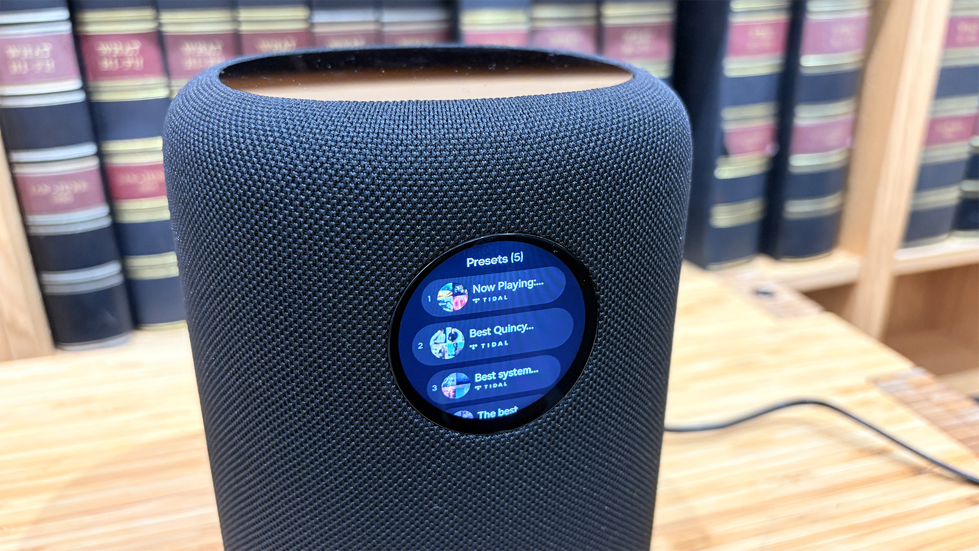 WiiM Sound wireless speaker in front of bookcase with track listings on round display screen