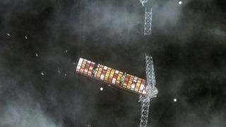 Aerial photo of a large cargo vessel as it crashes into the Francis Scott Key Bridge in Baltimore, Maryland, prompting its collapse.