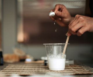 A pair of hands pouring baking soda to a water cup