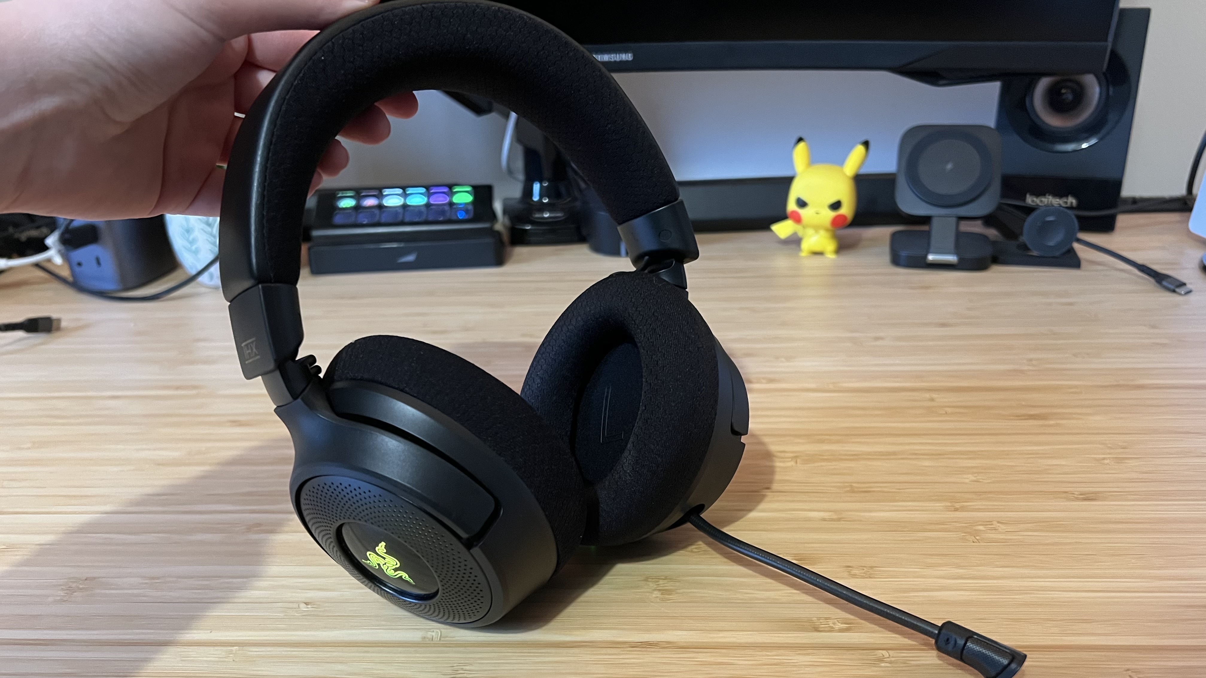 Hand holding Razer Kraken V4 up on a wooden desk with microphone extended