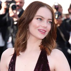 Emma Stone looks away from the camera wearing a plunging maroon dress