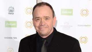 Todd Carty at a press event wearing a dark suit and shirt