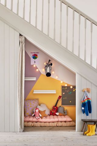 Playroom ideas fitted in under the stairs, with colorful walls, string lights and pink patterned floor cushions.