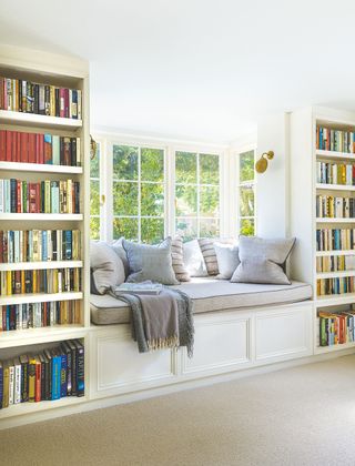 library with bay window seat and fitted bookshelves either side with view of gardend