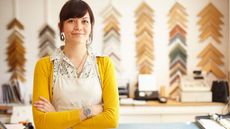 A woman who owns a frame shop stands in her store with arms crossed.